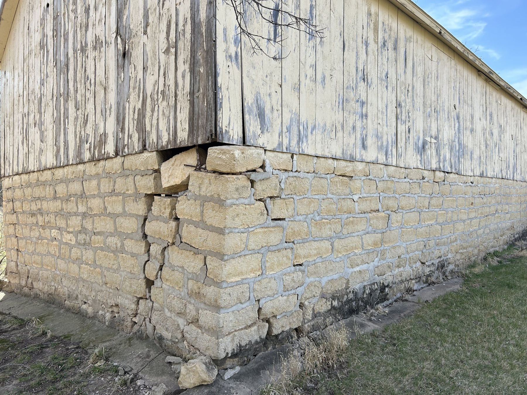 The same limestone barn corner before repair, with failed joints and dropped units
