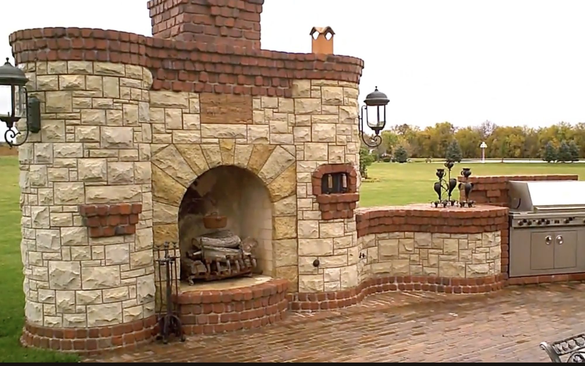 Outdoor fireplace with brick oven, round stone turrets, red brick soldier course, and a built-in gas grill